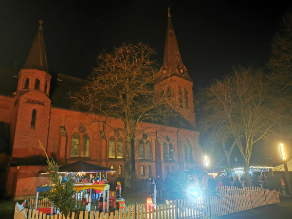 Ummelner Kirche im Dunkeln, davor Weihnachtsmarktstände und Menschen