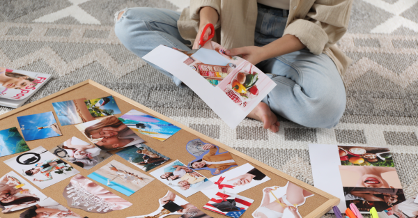 Eine Person sitzt barfuß im Schneidersitz auf einem Teppich und gestaltet ein Vision Board.