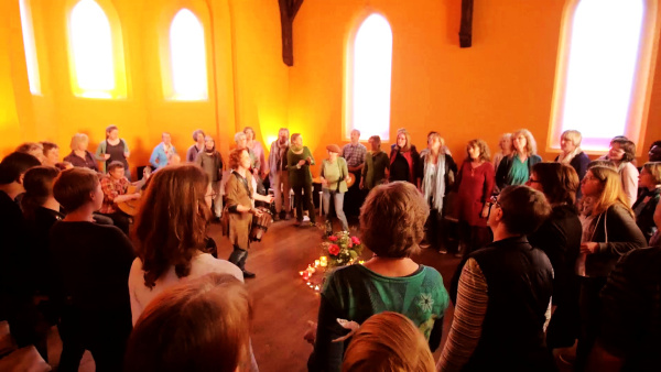 Das Bild zeigt den Innenraum der Capella hospitalis mit vielen singenden Menschen im Kreis.